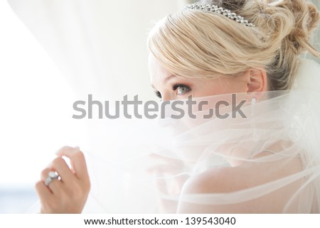 Gorgeous Smiling Blonde Bride In Front Of A Penthouse Window At A Modern Hotel Peaking Over Her Veil