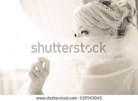 Gorgeous smiling blonde bride  in front of a Penthouse window at a modern hotel peaking over her veil