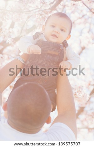 Father lifting his son into the sun for a sun flared softened portrait of a Happy Baby