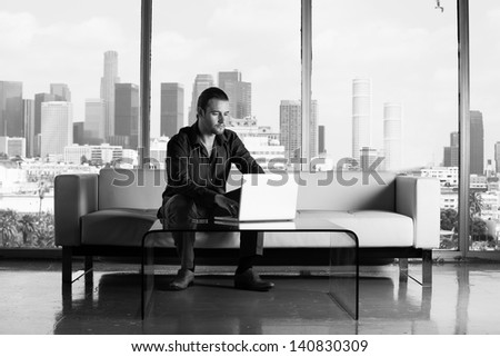 Young handsome casual business man working in a Penthouse Suite with Los Angeles Skyline behind him Black and White Image