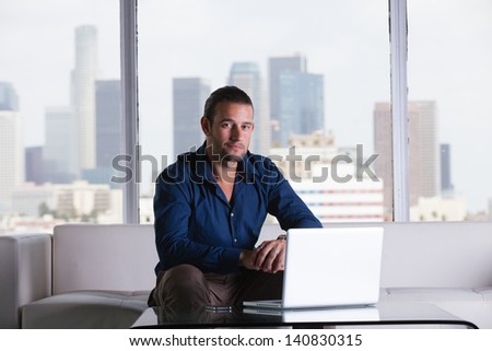 Young handsome casual business man working in a Penthouse Suite with Los Angeles Skyline behind him