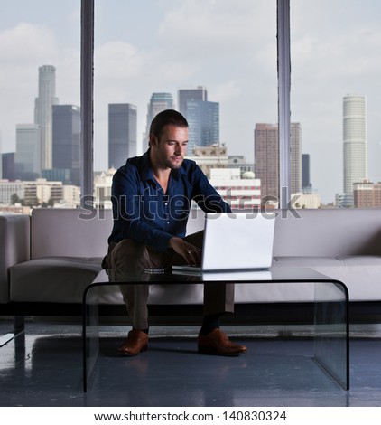 Young handsome casual business man working in a Penthouse Suite with Los Angeles Skyline behind him