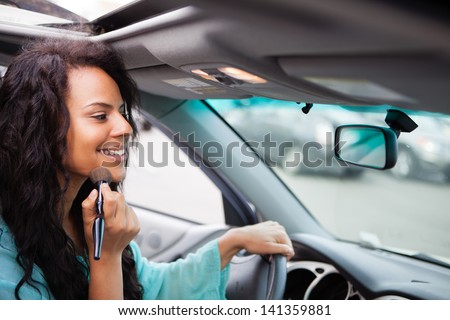 Attractive young woman touching up her make up in a Car looking in the rear view mirror