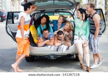 Attractive Group of young People gathered around an SUV at the Beach having fun Laughing and talking