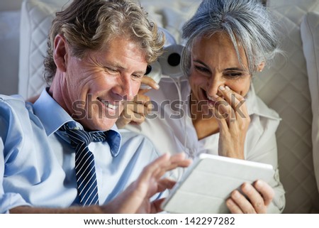 Attractive Mature couple listening to music on Headsets from a Mini touch Pad on a bed after work