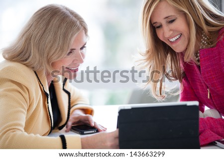 Two attractive mature women  sharing ideas on a touch pad in a penthouse