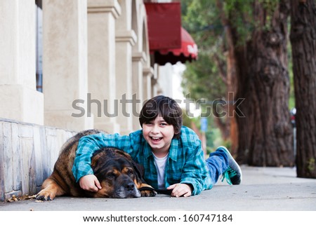 A 10 year old boy and his dog lying down on the sidewalk