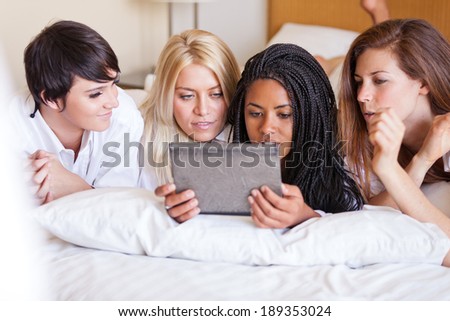 Four Beautiful friends sharing pictures on a touch screen while snuggled all in white on a hotel bed