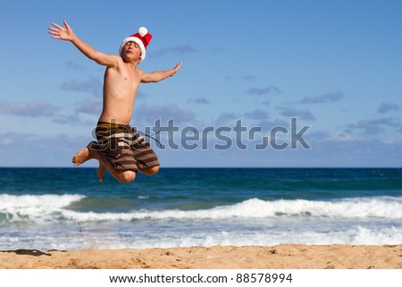 stock photo A Teen Boy Wearing a Santa Hat Jumping on the Beach in Hawaii