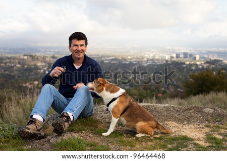 Handsome Man on a Hill Top with his Dog and a treat City in the background