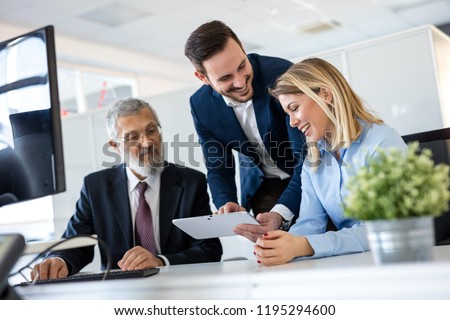 Smiling young manager helping senior worker with funny computer work in office, mentor teacher training happy older employee at workplace, colleagues of different age laughing looking at pc monitor.