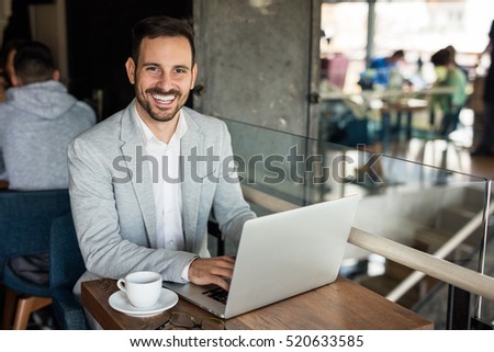 Handsome businessman using laptop at city cafe. Toothy smile.