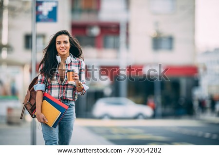 Young talented female student dressed in casual clothing walking around city and listening to favorite radio station via earphones. Attractive brunette woman enjoying free time outdoors with music.