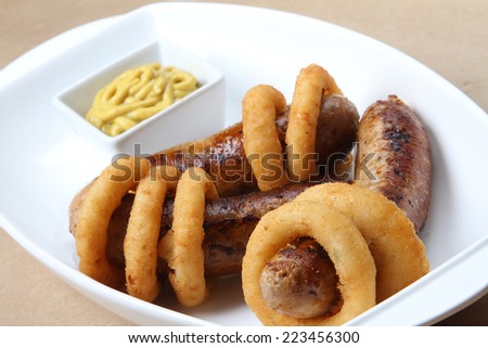 spicy American grilled sausages served on a white plate with spicy sauces and delicious baked potatoes and crunchy onion rings ketchup  mustard