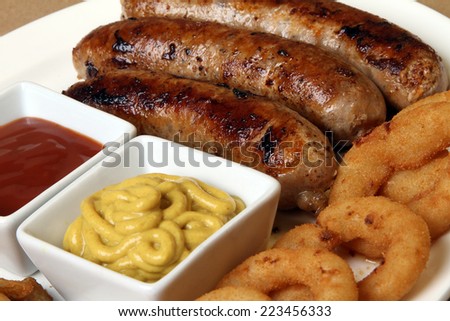 spicy American grilled sausages served on a white plate with two spicy sauces and delicious baked potatoes and crunchy onion rings ketchup  mustard