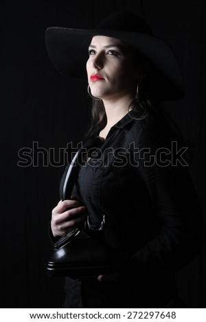 beautiful young brunette woman lady posing in a studio on a black background with old style hat  holding a telephone