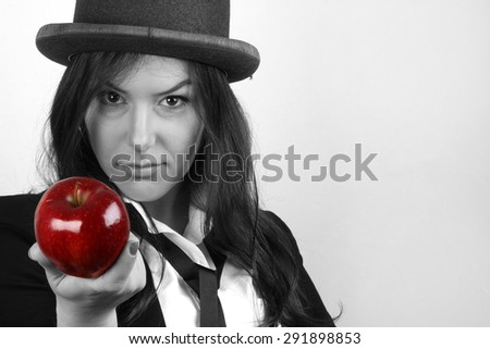 Girl and apple - Beautiful young brunette with red nail polish and a bowler hat on her head in a white shirt with a black tie in a black jacket holding a red organic fresh apple in hands provocative