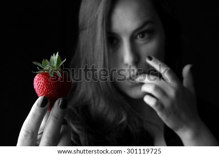 Girl and strawberries - beautiful young brunette with big breasts posing with a red fresh organic strawberries and seductive and sexy looking into the camera - black and white studio shoot