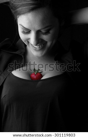 Girl and strawberries - beautiful young brunette with big breasts posing with a red fresh organic strawberries and seductive and sexy looking into the camera - black and white studio shoot
