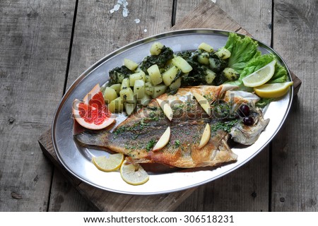 fish served as a meal for the restaurant with herbs and boiled potatoes as a side dish - rustic wooden background - Bass, European seabass, lubin, brancin, smudut, Wolfbarsch