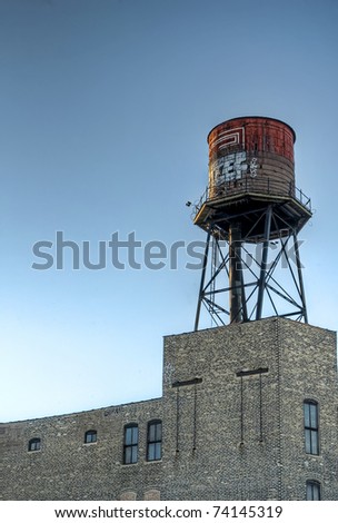 An old graffiti covered water tower over a blue late afternoon sky