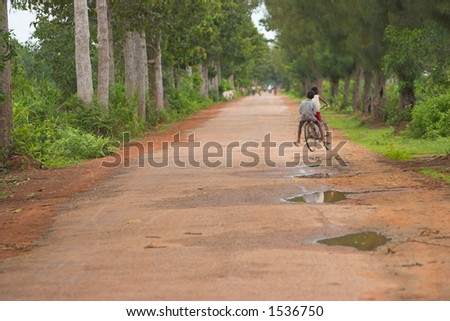 two children friends riding on a bicycle on a dirt road in tropical country