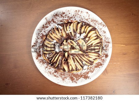 Chocolate and pear cake, view from above, made with pear slices aligned all around in the top and sugar on top. Image in light desaturation and vintage style