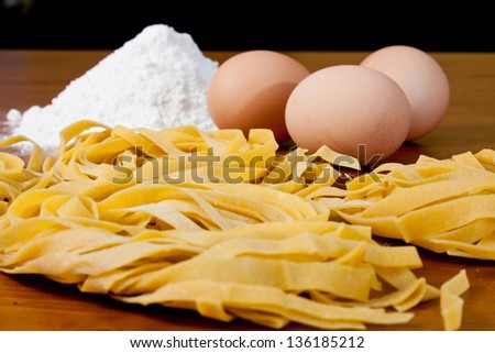 Home-made pasta and ingredients, with flour and eggs over a wooden table.