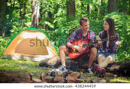 Young couple playing on guitar in the forest.\
Camping, hiking.