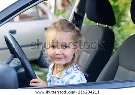 Happy little  girl sitting of car on driver seat holding steering wheel