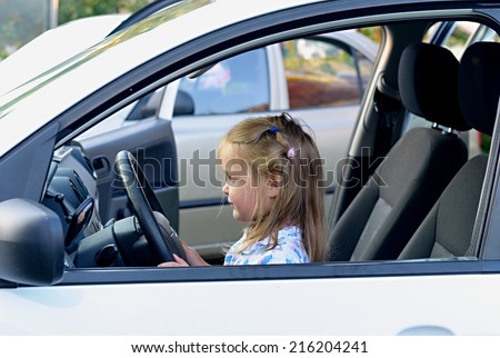Happy little child, funny blonde little girl sitting of the car on driver seat holding steering wheel