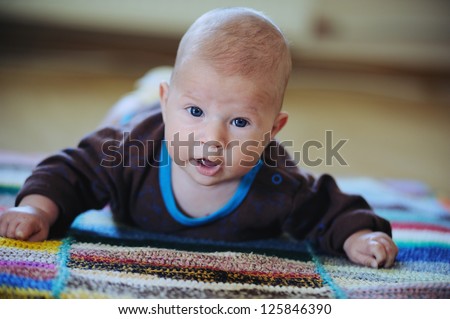 Adorable three month baby crawling on colorful blankets on the warm floor