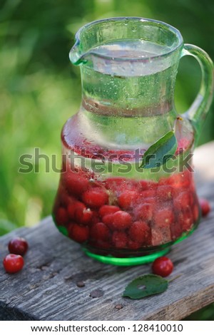 Jug of cold fresh water with cherries on wooden table in the garden