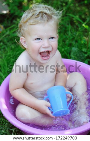 Beautiful little boy playing in a bowl of water in the summer garden