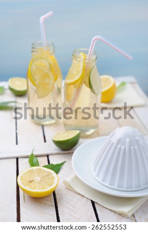 Fresh lime and lemon, squeezer and two glasses of lemonade on rustic table