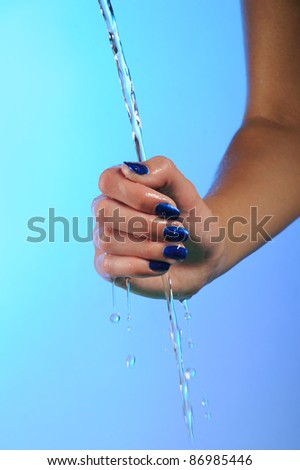 hands with woman\'s blue nails manicure and stream clean water