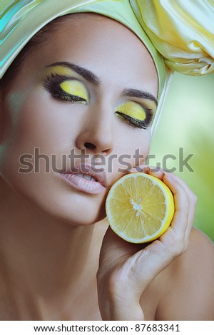 beautiful woman with lemon in yellow scarf on her head and bright makeup on closed eyes