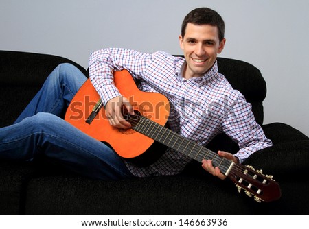 A young adult happy with guitar, on the couch / On the couch with guitar