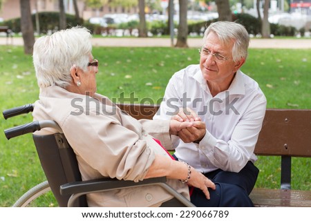 Man holding the hand of a senior woman in wheel chair talking at the park