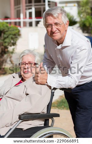 Man with thumb up walking with senior woman in a wheelchair