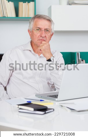 Mature man looking at camera with laptop in his office