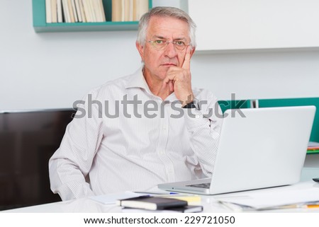 Mature man looking at camera with laptop in his office