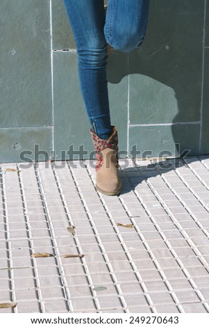 Legs of urban girl with jeans and boots standing in front of a stone wall