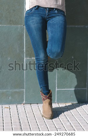 Legs of urban girl with jeans and boots standing in front of a stone wall