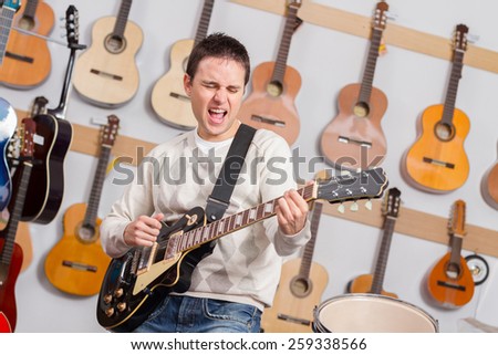 Man singing and playing electric guitar in music shop