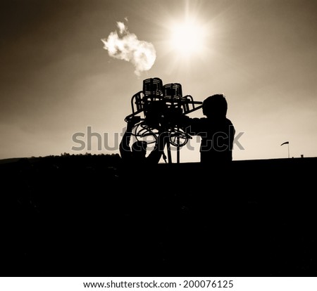 black silhouette of two men holding hot air balloon burners against the sun