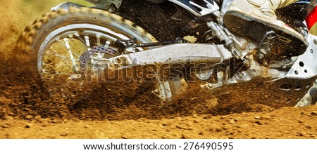 Motocross machine wheel and raised dust captured right after the motocross race machine starts off, no recognizable people, motion blur