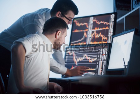Team of stockbrokers are having a conversation in a dark office with display screens. Analyzing data, graphs and reports for investment purposes. Creative teamwork traders.