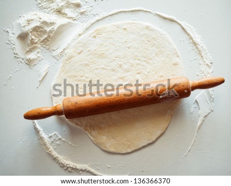 Block of freshly made pastry rolled out on a floured work surface with a wooden rolling pin