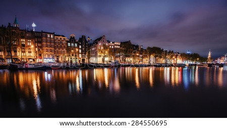 Beautiful night in Amsterdam. Night illumination of buildings and boats near the water in the canal.